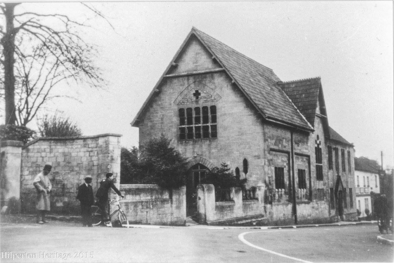 A tall gabled stone building standing directly on the road, with children in front of it.