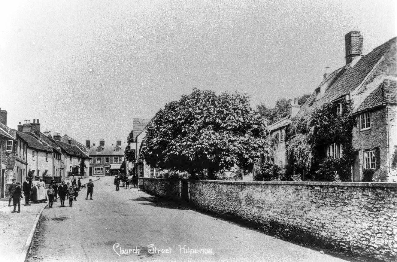 A printed postcard view along Church Street, with a long rubble wall on the right and a group of figures in the distance.