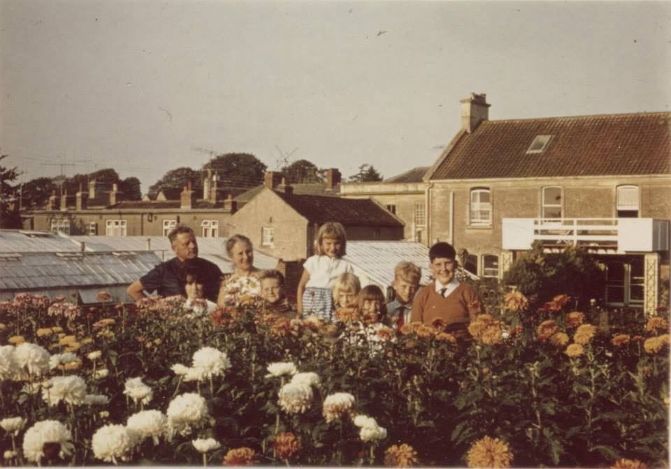 A group standing in the flower beds behind the house, with blooms in the foreground.