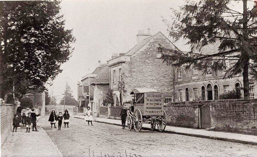Villagers and a hand cart in the middle of the road, with the raised pavement and boundary wall behind.